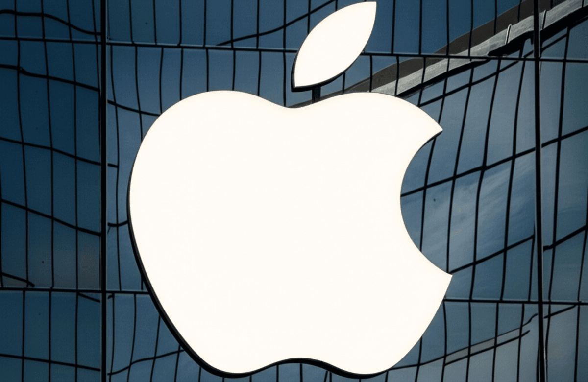 The iconic white Apple logo, illuminated from within, is mounted on a modern facade of large, gray-blue rectangular panels.